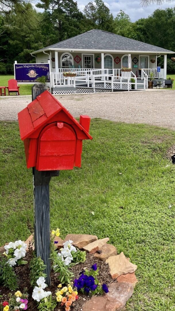 Red mailbox with flowers in front of shop.